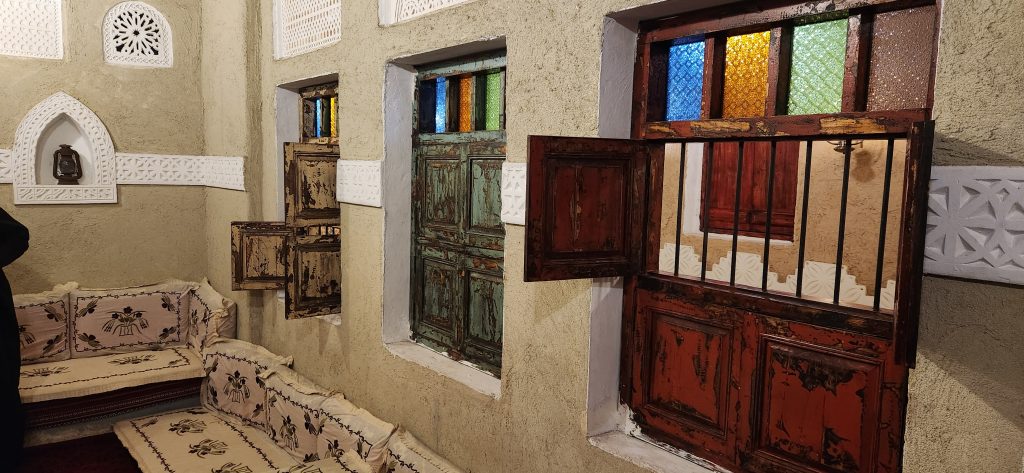 Restored interior of a traditional Saudi home featuring ornate wooden doors, colorful stained glass windows, and decorative wall patterns, highlighting Saudi Arabia's domestic heritage.