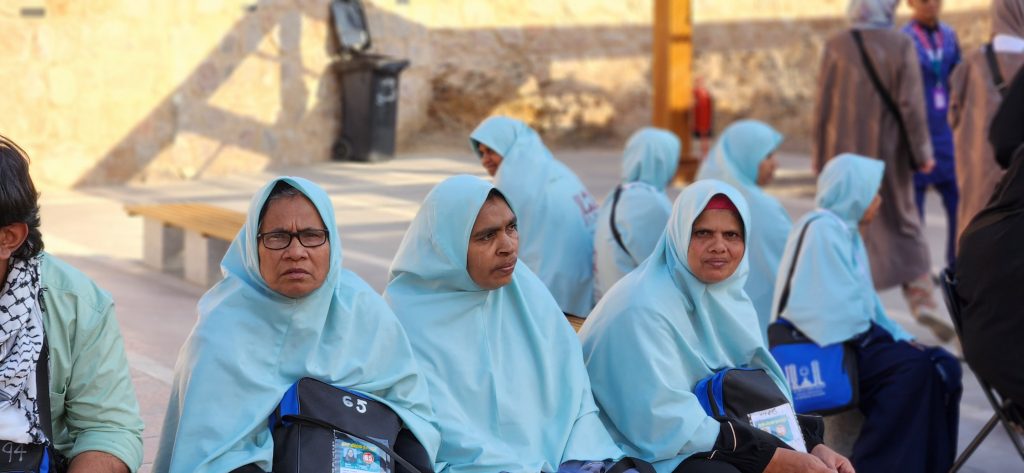 Women in light blue hijabs sitting together, reflecting the cultural attire during a visit to a significant site in Saudi Arabia, amidst a backdrop of other visitors.