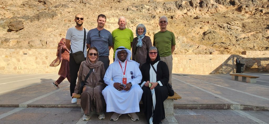 Group of travelers and a local guide posing for a photo in Saudi Arabia, with rocky terrain in the background, capturing a moment of camaraderie after exploring the region.
