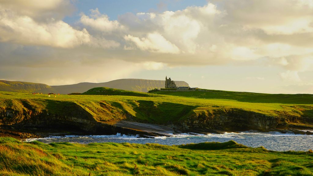 Irish landscape featuring rolling green hills, a distant castle, and a coastline with waves, highlighting Ireland's natural beauty and cultural heritage.