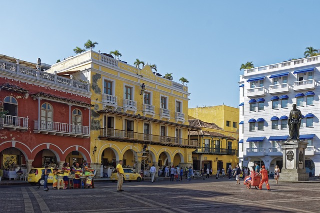 Colorful colonial buildings in Cartagena's vibrant plaza, featuring a statue and people enjoying the lively atmosphere, representing relaxed coastal escapes and cultural experiences in luxury travel.
