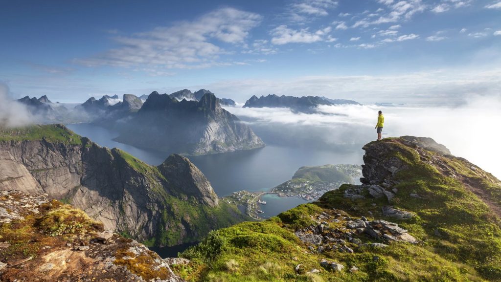 Person standing on a rocky outcrop overlooking a breathtaking fjord landscape in Norway, showcasing the stunning natural beauty and adventurous spirit of off-the-beaten-path travel experiences.
