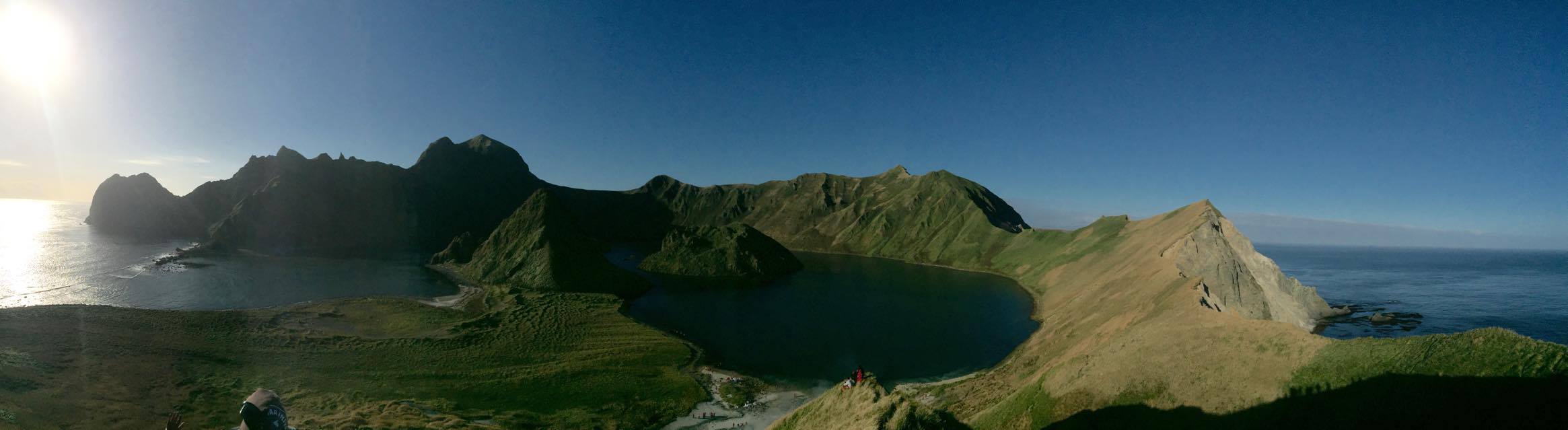 Panoramic view of a serene coastal landscape with lush green hills, rocky cliffs, and a tranquil blue sea under a clear sky, reflecting Richard's focus on off-the-beaten-track travel experiences.